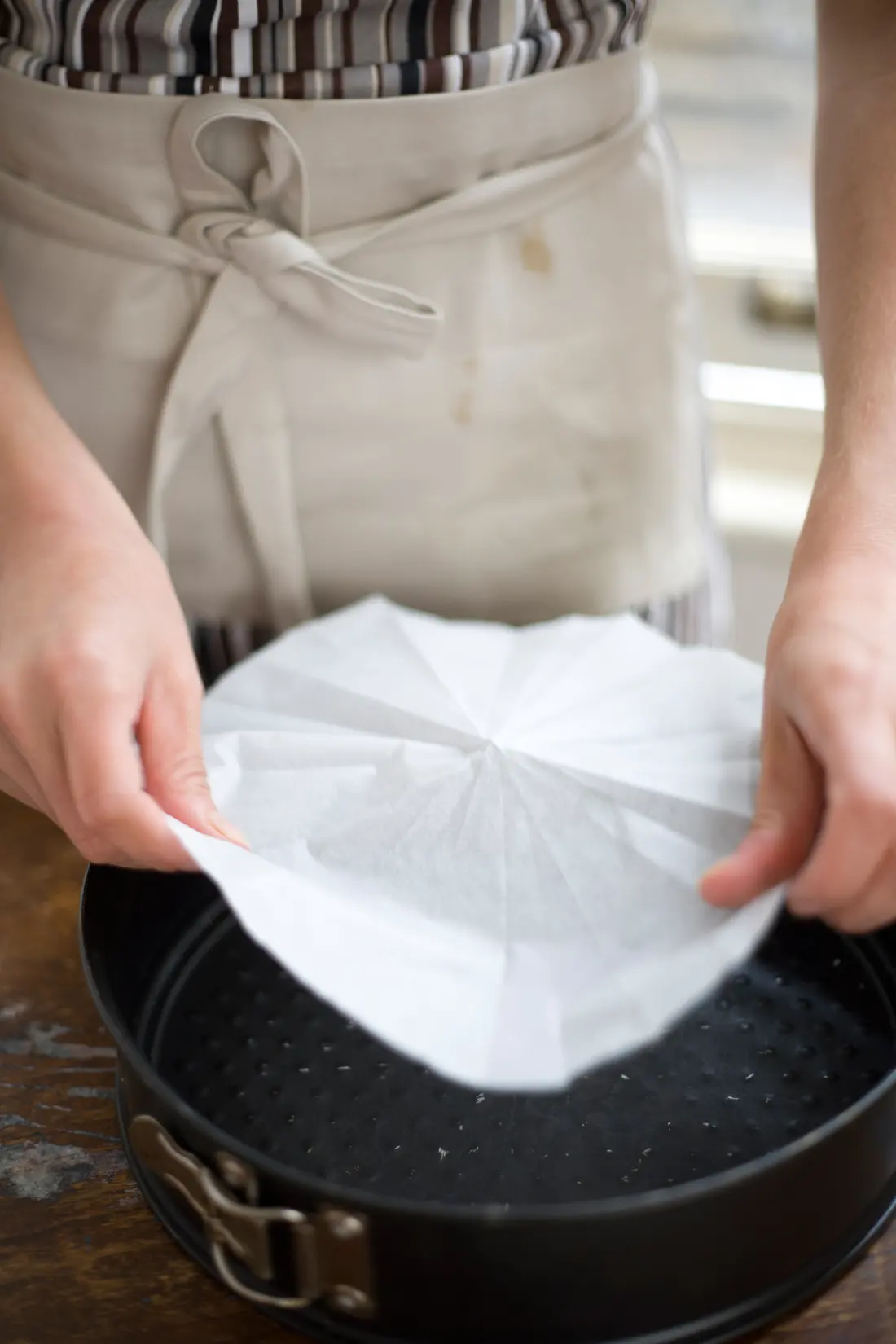 Hands lining a springform cake tin with baking parchment