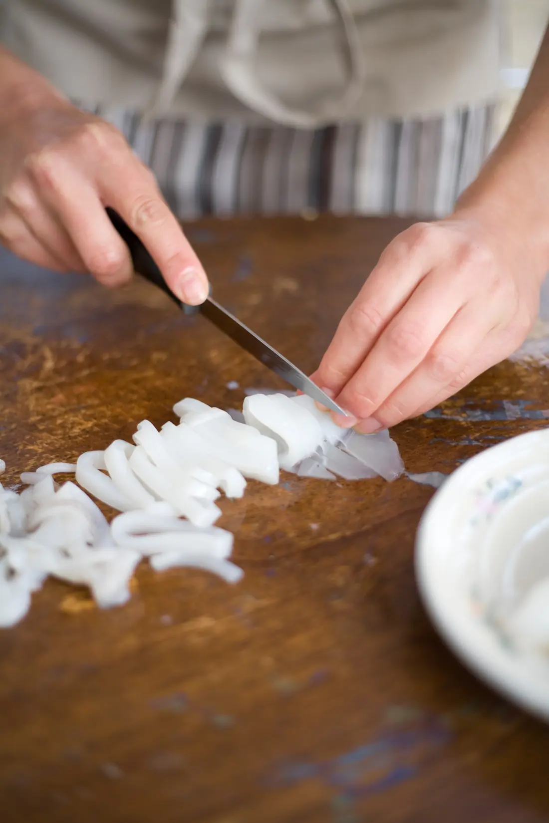 Hands chopping onion with a knife on a wooden board