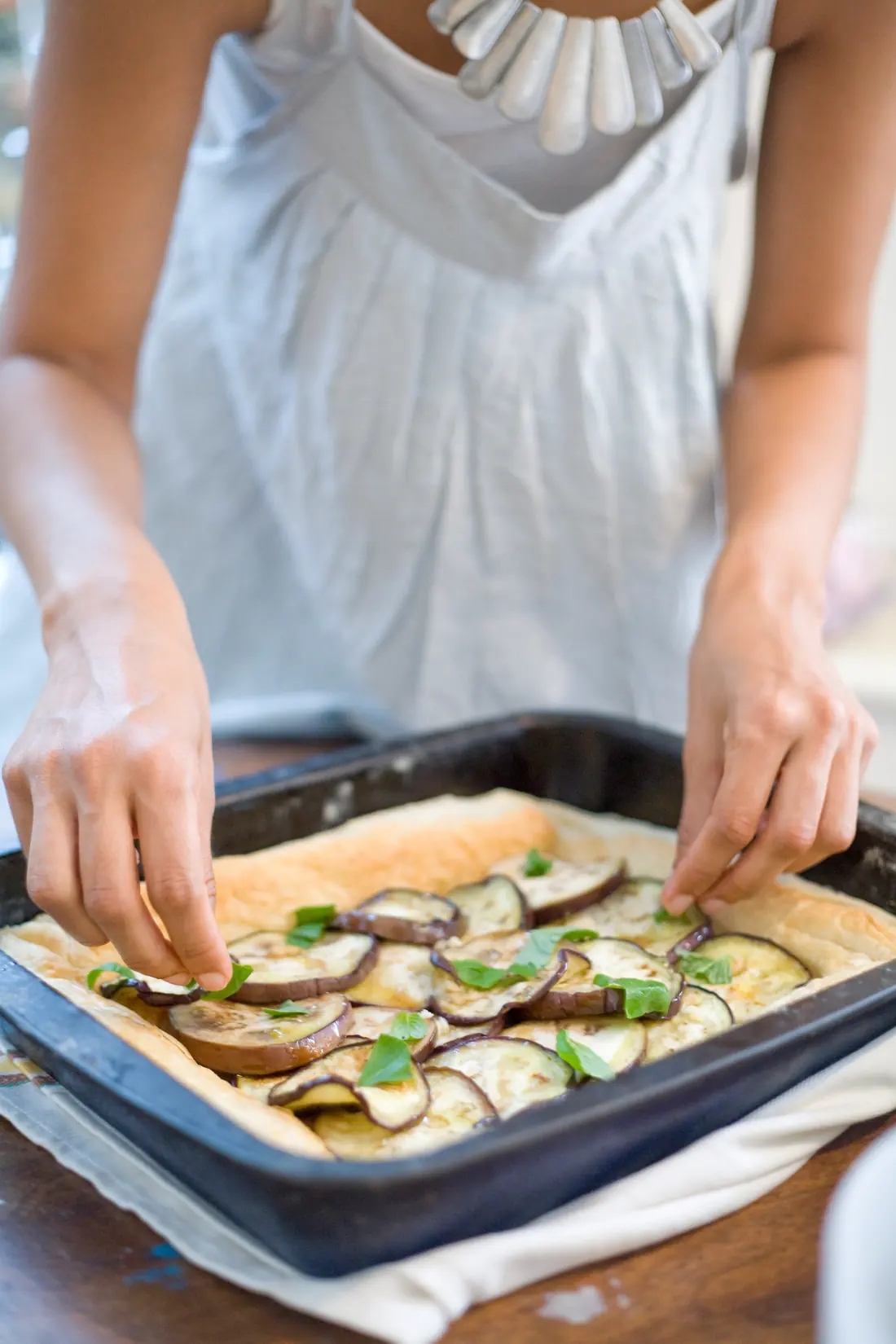 Hands laying aubergine slices over pastry